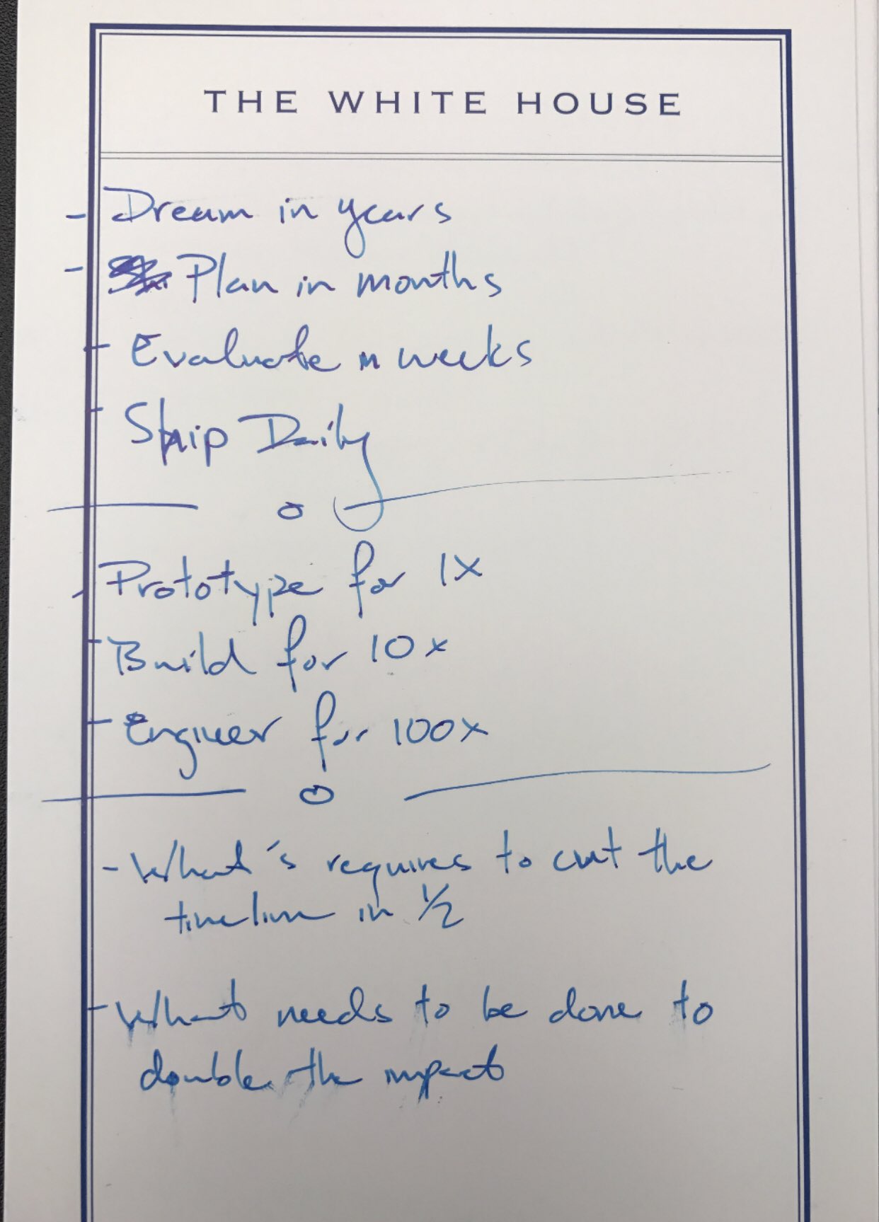 A piece of notepaper with the White House letter heading on it that has a hand-scribbled note that reads: Dream in years, plan in months, evaluate in weeks, ship daily. Prototype for 1x, Build for 10x, Engineer for 100x. What's required to cut the timeline in half? and What needs to be done to double the impact?